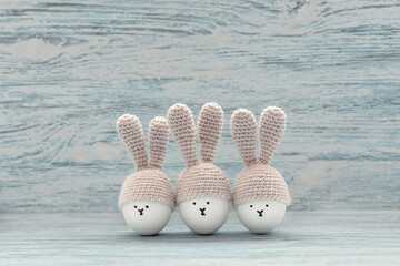 Three Easter eggs in crochet hats with bunny ears against painted shabby wooden background