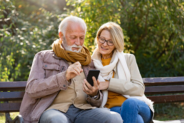 Cheerful elderly couple using banking apps on a smartphone to make payments outdoors in the park