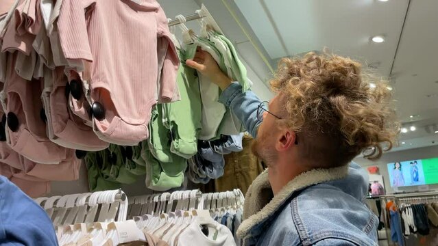 Man chooses gift clothes for small child in clothing store. Consulting with his wife by sending photo from smartphone typing message. The concept of caring loving father, uncle, brother relative