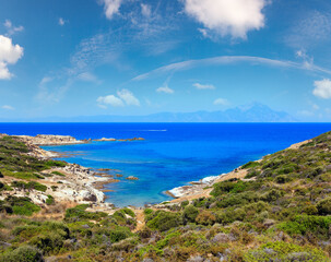 Fototapeta na wymiar Summer stony sea coast landscape with Atthos mount view in far (Halkidiki, Sithonia, Greece).
