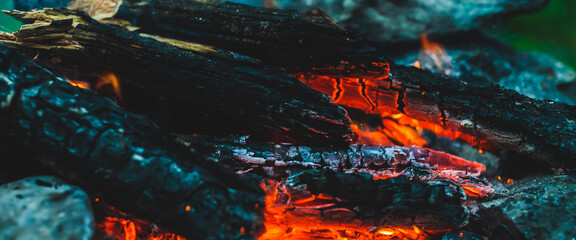 Vivid smoldered firewoods burned in fire close-up. Atmospheric warm background with orange flame of...