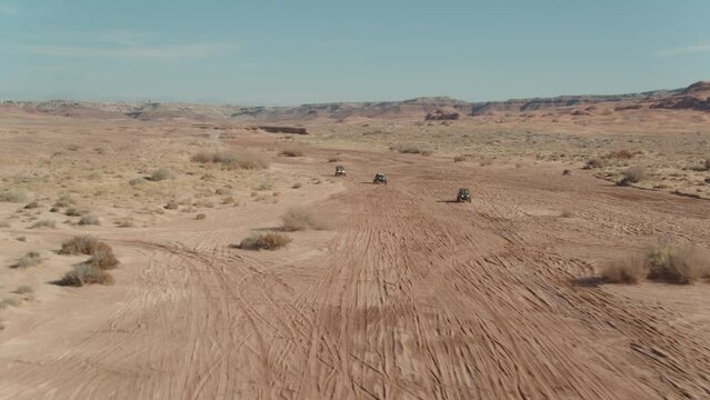 Aerial leading UTVs driving through red sand wash in Utah desert with beautiful sandstone canyon walls