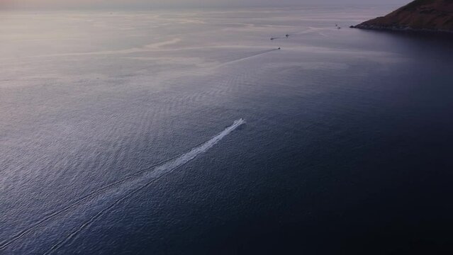 Tourist is riding jet ski in the sea near rocky shoreline in Thailand filmed by drone in the evening. Aerial view of hydrocycle moving in the ocean next to green island. Active summer vacations theme.