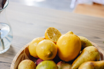 Close up of bright yellow lemon in wooden bowl, surrounded by fruit on kitchen counter