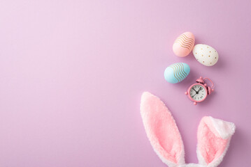 Easter concept. Top view photo of fluffy bunny ears colorful easter eggs and pink alarm clock on...
