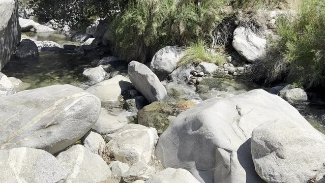 A clear stream flows away across smooth boulders in the sun