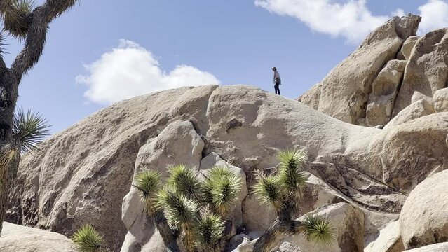 Man walks up a large desert rock against a brilliant blue sky 