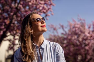 Beautiful smiling woman on the background of lilac pink cherry blossoms