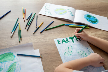 A child at school at the table draws the planet Earth with a world map with multi-colored pencils...