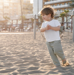 Baby boy running shoeless on sand beach in sunset light wearing white t-shirt and long trousers in South Spain in Summer