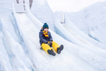 happy boy slides down an ice slide in winter outside	
