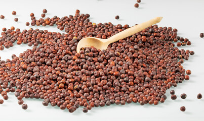 A large pile of dark peas on a light background with a wooden spoon on top
