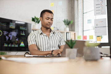 Portrait of attractive young businessman sitting at office desk and working with laptop. African american guy having online video conference. Business meeting online.