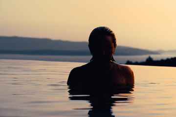Fototapeta premium Girl at sunset in the pool. In the background, the sea and mountains.