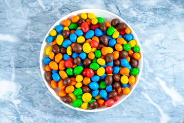 Multi-colored round candies in colored glaze in large quantities in a plate
