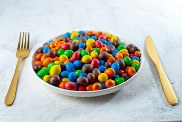 Multi-colored round candies in colored glaze in large quantities in a plate