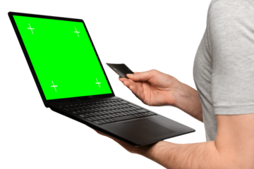 A man in a T-shirt holds a laptop, an ultrabook and a bank card with his second hand, makes an online purchase.
