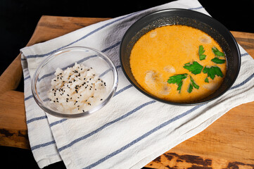 Tom yum soup in a bowl and with a bowl of rice lie on a cloth napkin and a wooden tray. exotic healthy asian food