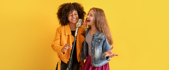 Teenage girls singing in microphone against yellow background