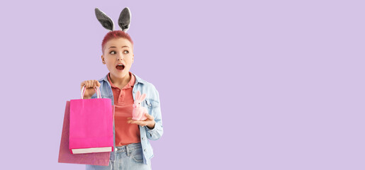 Surprised young woman with shopping bags and Easter bunny on lilac background with space for text
