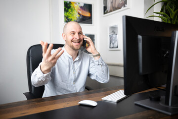 Man with bald head gesticulating on phone in office/home office with friendly face he is in a...