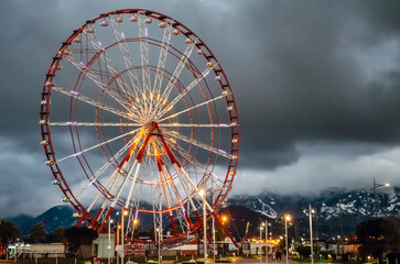 Ferris wheel in the evening, attraction, cloudy weather, clouds and mountains on the background