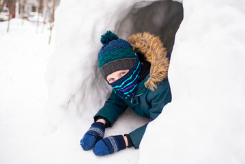 happy laughing schoolboy in snow cave in winter outside