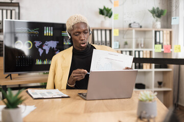 Serious marketing african man in suit and headset talking to client on video call, presenting paper graphic reports, showing, explaining diagram. Employee, manager attending online meeting