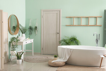 Interior of bathroom with modern bathtub, ceramic sink and houseplants near green wall
