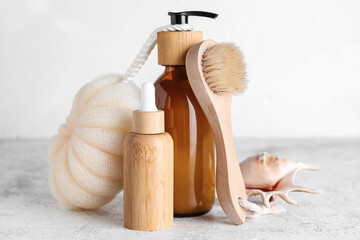 Bottles of cosmetic products, sponge, massage brush and seashell on light background