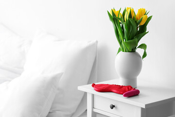 Vibrator, sleeping mask and vase with tulips on table in bedroom