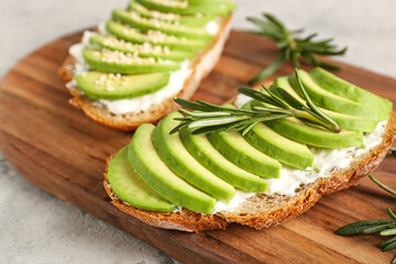 Board with delicious avocado toasts and rosemary on grey background