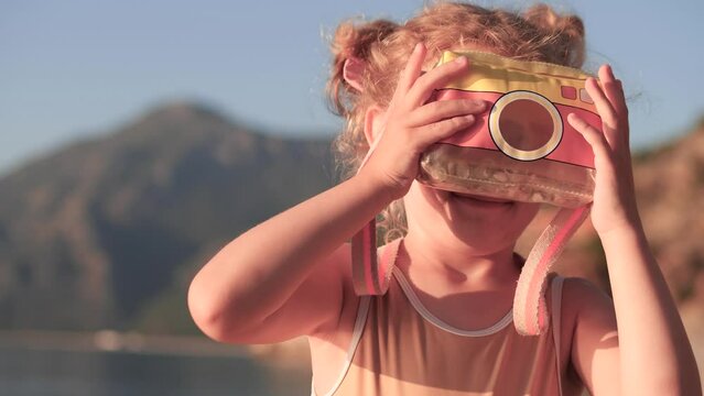 Happy little girl makes photos with a toy camera on a beach on a summer day