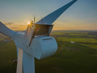 Nacelle roof of a wind turbine with fields in the backgroundagainst the sun.Aerial view of countryside with a close-up of a wind turbine as seen from the nacelle (hub) against sun. - obrazy, fototapety, plakaty