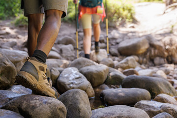 Low section of diverse couple trekking in sunny wilderness, walking along rocky riverbed