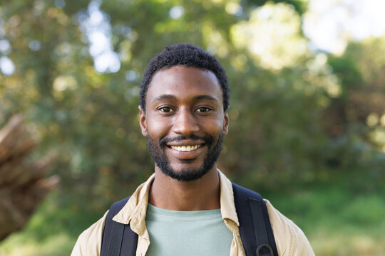 Portrait of happy african american man trekking in forest with backpack, smiling, copy space