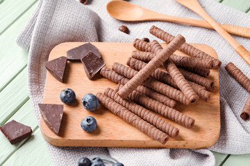 Board with delicious wafer rolls, blueberries and chocolate pieces on green wooden background