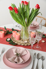 Table setting for International Women's Day celebration with tulip flowers, burning candles and eucalyptus branches in light room