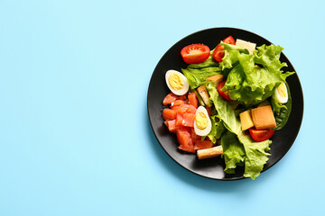Plate of delicious salad with boiled eggs and salmon on blue background