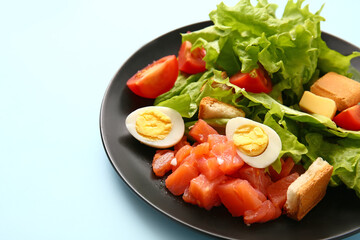 Plate of delicious salad with boiled eggs and salmon on blue background