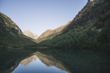 Fototapeta na wymiar Morning landscape in the mountains with a lake in a valley between mountain slopes and rocks with a forest, a mirror surface of a mountain lake in the morning