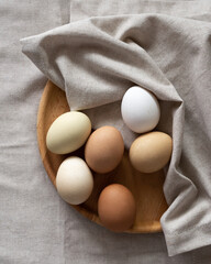 Nature colors Easter eggs. Eggs on a wooden plate on a beige napkin. A chicken egg as a valuable nutritious product. Top view flat lay