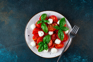 Italian caprese salad with sliced tomatoes, mozzarella, basil, olive oil on a dark background. Top view. Italian food. Healthy salad. Summer food