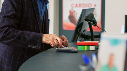 Obraz premium Elderly man paying for supplements with credit card, woman pharmacist handing out shopping bag with prescription treatment. Person using contactless payment on pos terminal. Handheld shot.
