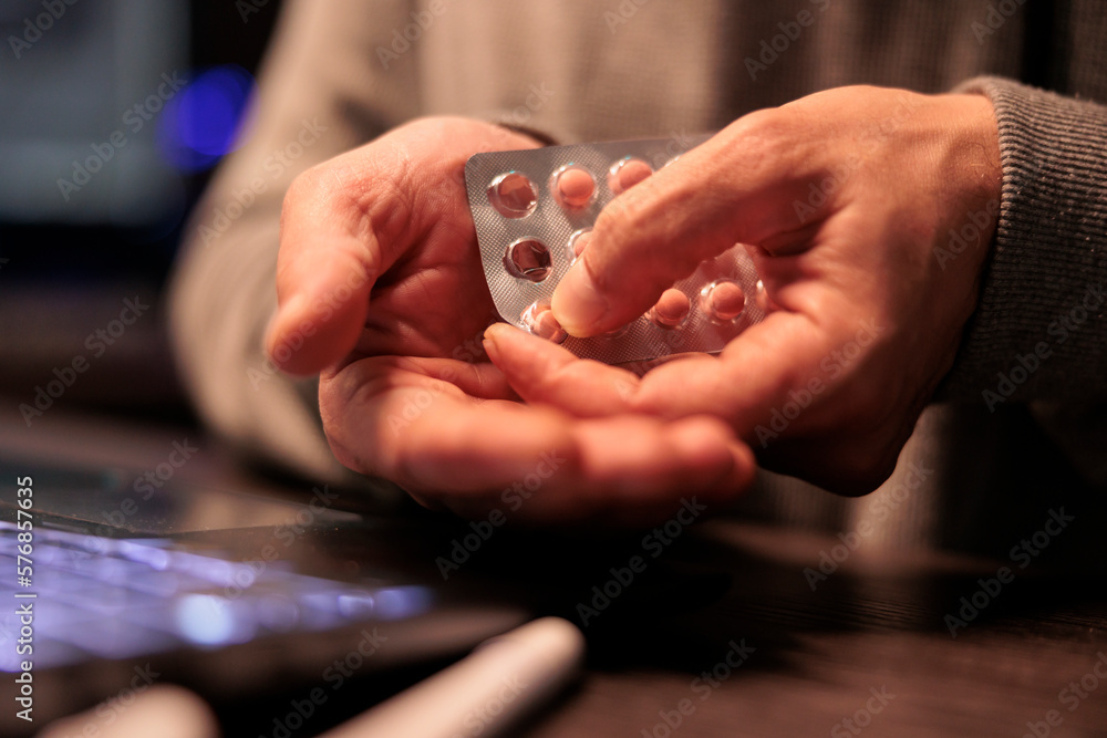 Poster young programmer taking pills and vitamins from foil, feeling stressed working after hours in app de