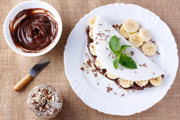 homemade tapioca or beiju stuffed with banana and chocolate on white plate over rustic wooden table