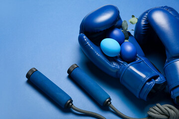 Boxing gloves with Easter eggs, eucalyptus and skipping rope on blue background, closeup