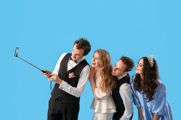 Beautiful couples dressed for prom taking selfie on blue background © Pixel-Shot