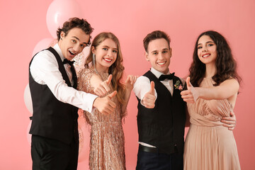 Beautiful couples dressed for prom showing thumb-up gesture on pink background - obrazy, fototapety, plakaty