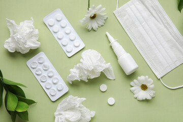 Nasal drops with pills, flowers, medical mask and tissues on green background. Seasonal allergy...